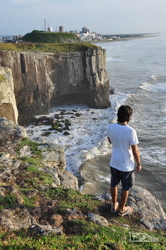 Do alto das falésias de pedra o João Pedro admira o mar de Torres, litoral norte do Rio Grande do Sul